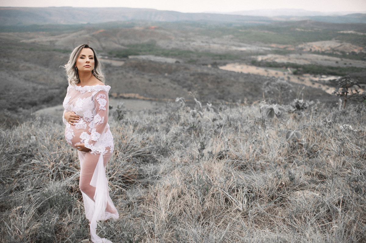 Gestante usando vestido branco transparente em uma vegetação cinza. Clicado pelo fotógrafo de gestantes Rafael Ohana em Brasília-DF