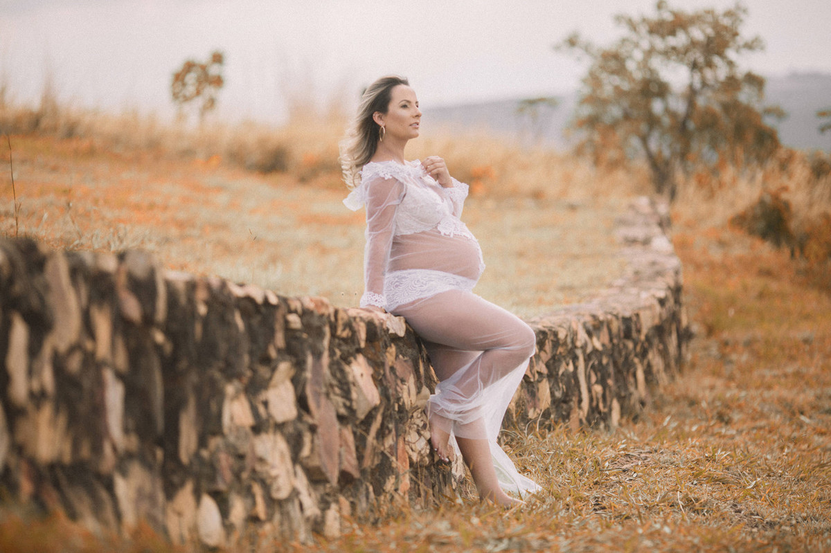 Gestante encostada no mudo de pedras usando vestido transparente. Clicado pelo fotógrafo de gestantes Rafael Ohana em Brasília-DF