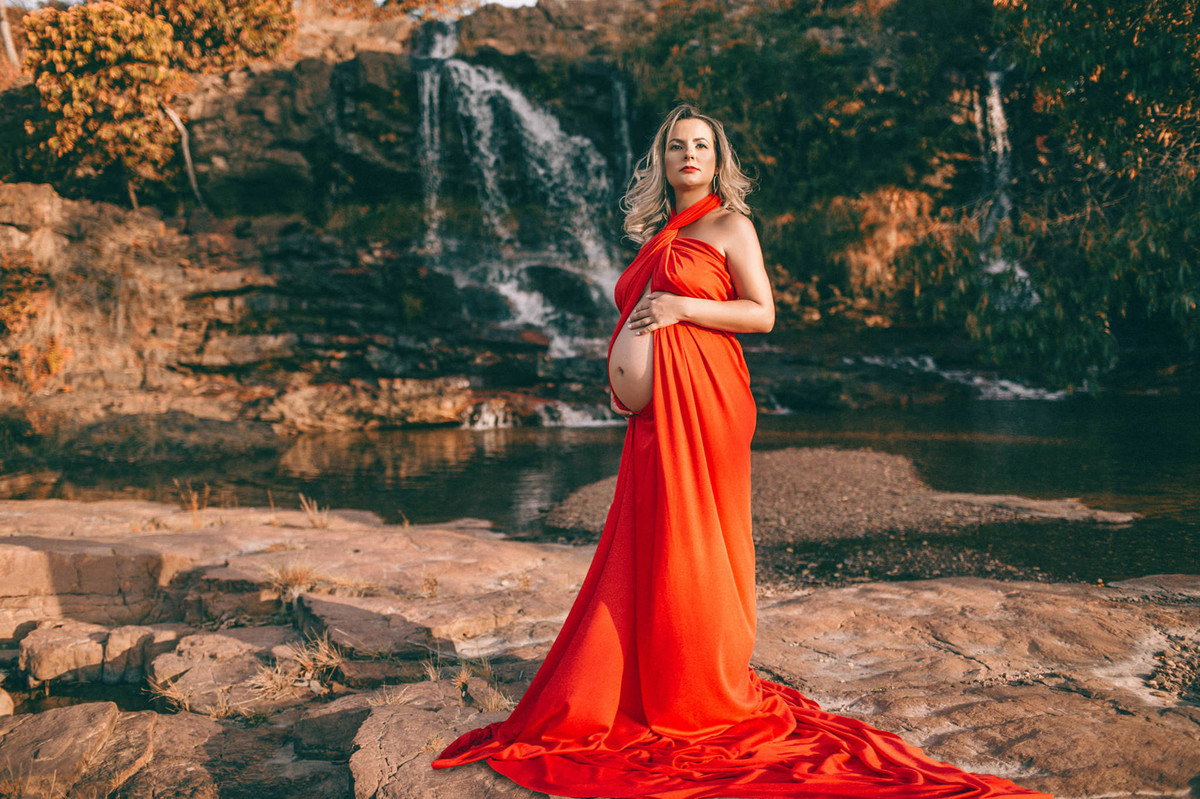 Grávida perto de cachoeira usando vestido vermelho com barriga à mostra. Clicado pelo fotógrafo de gestantes Rafael Ohana em Brasília-DF