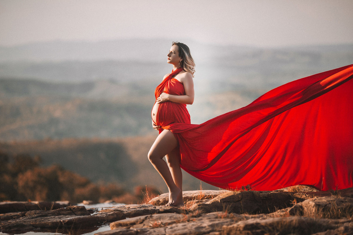 Grávida posando maravilhosa com seu vestido vermelho esvoaçante perto de montanhas. Clicado pelo fotógrafo de gestantes Rafael Ohana em Brasília-DF