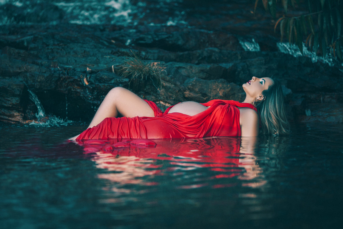 Gestante dentro da agua da cachoeira com vestido vermelho molhado. Clicado pelo fotógrafo de gestantes Rafael Ohana em Brasília-DF