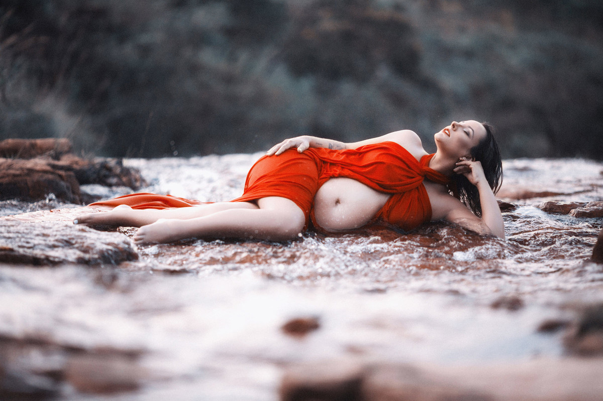 Grávida relaxando nas pedras do rio com seu vestido vermelho incrível. Clicado pelo fotógrafo de gestantes Rafael Ohana em Brasília-DF