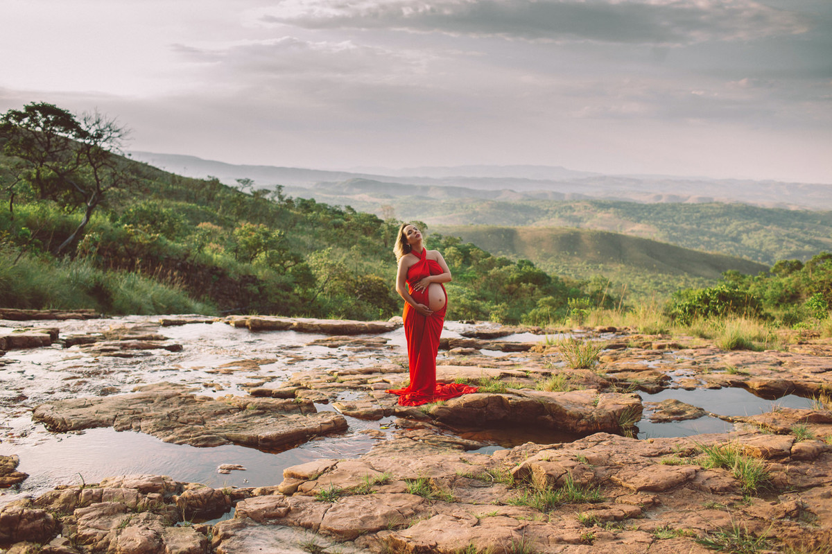 Grávida posando com seu vestido vermelho nas pedras do rio. Clicado pelo fotógrafo de gestantes Rafael Ohana em Brasília-DF