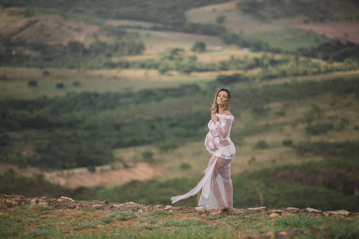 Loira grávida usando vestido branco transparente perto de um precipício. Clicado pelo fotógrafo de gestantes Rafael Ohana em Brasília-DF