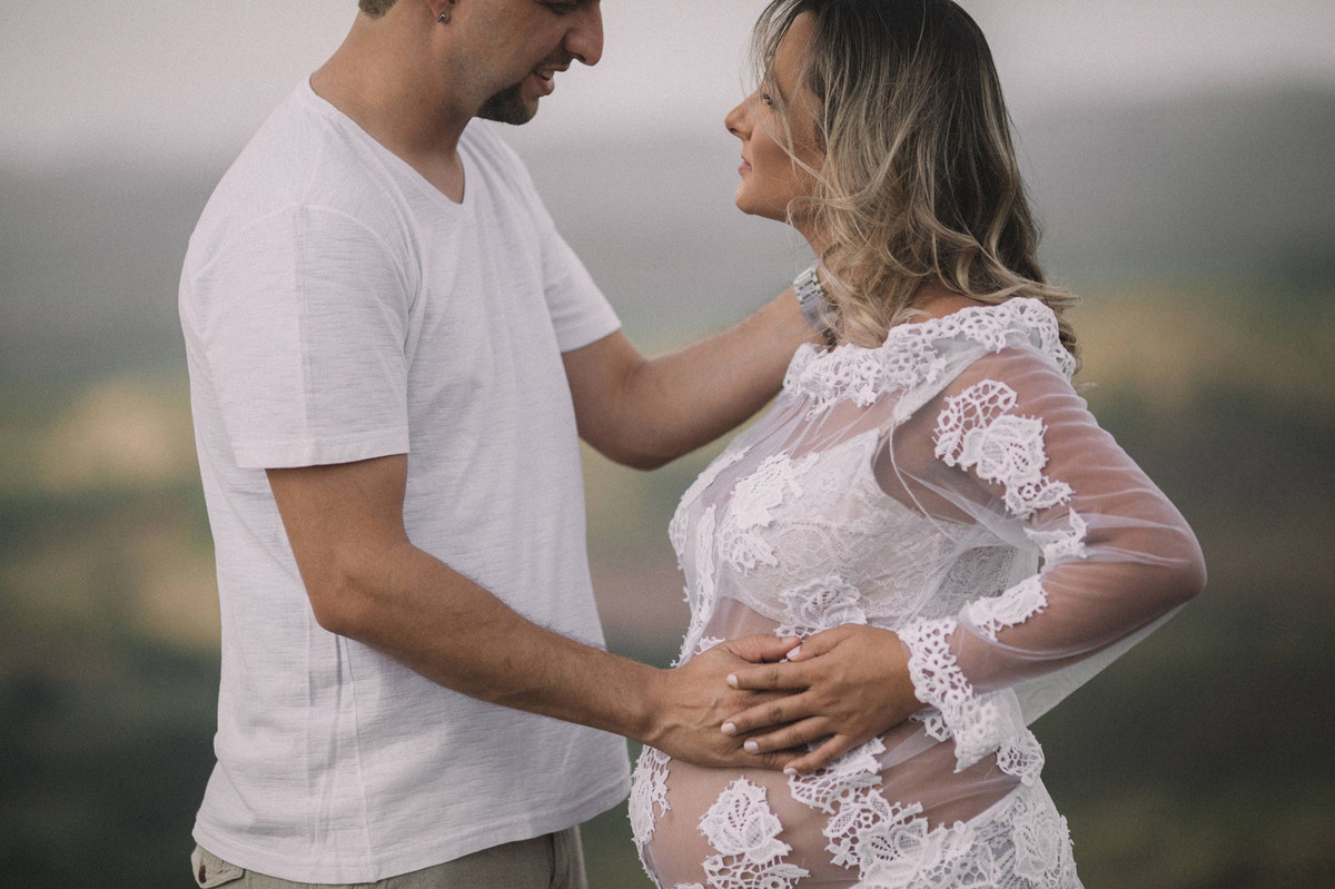 Gestante usando vestido branco transparente com seu marido na natureza. Clicado pelo fotógrafo de gestantes Rafael Ohana em Brasília-DF