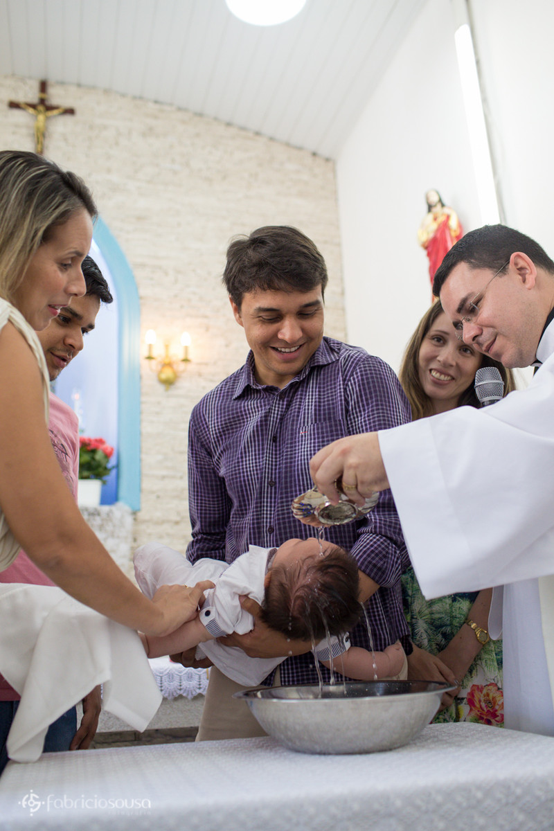 Erivelto segura o filho enquanto o padre despeja a água benta