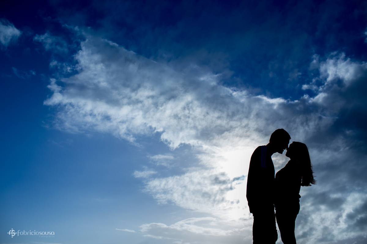 silhueta do casal quase se beijando com céu azul e muitas nuvens