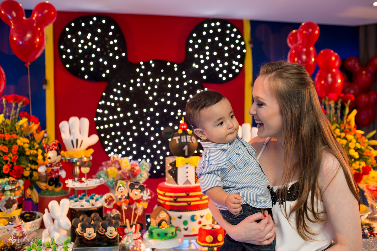 Mãe contente com Theo no colo em frente a mesa de doces