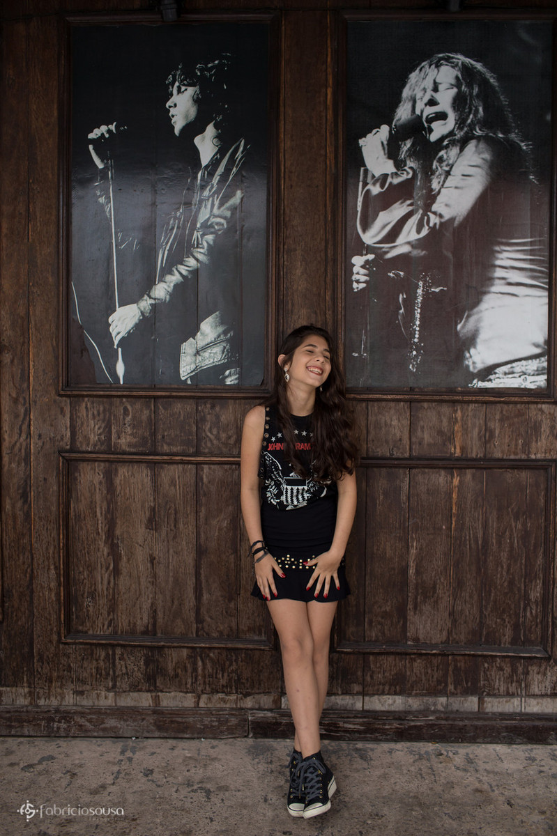 Juliana feliz com roupa preta estilo rock em frente de duas imagens de rockeiros famosos