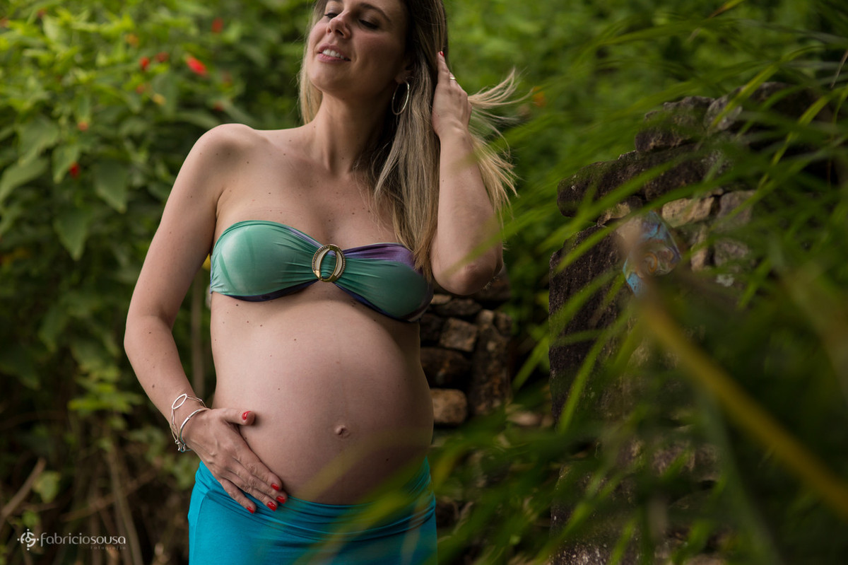 Mulher grávida de biquini mexendo no cabelo em meio a natureza
