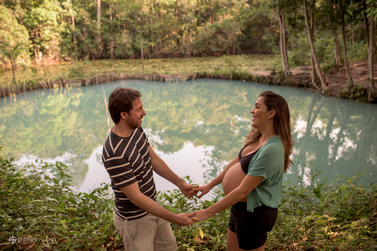 casal grávido de mãos dadas e lago verde de fundo