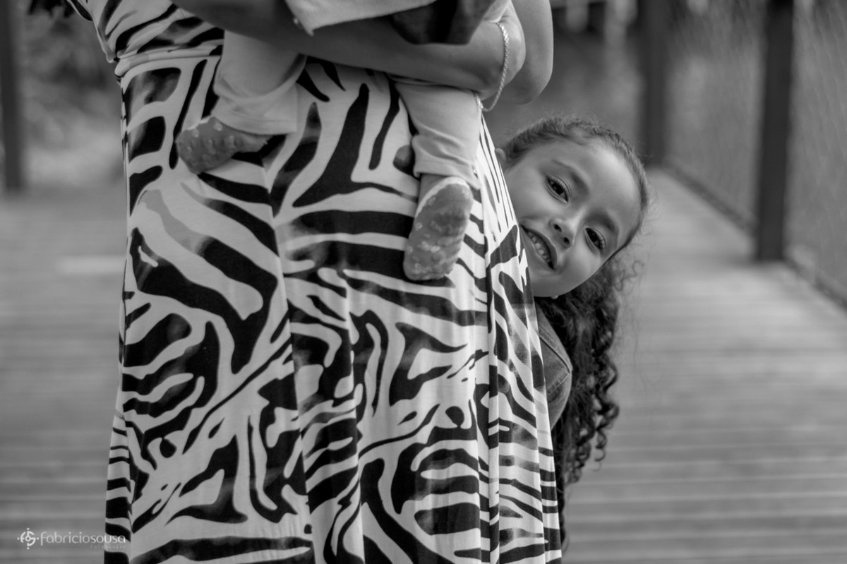 Mamãe segura filha pequena e a outra filha se esconde atrás do vestido pb