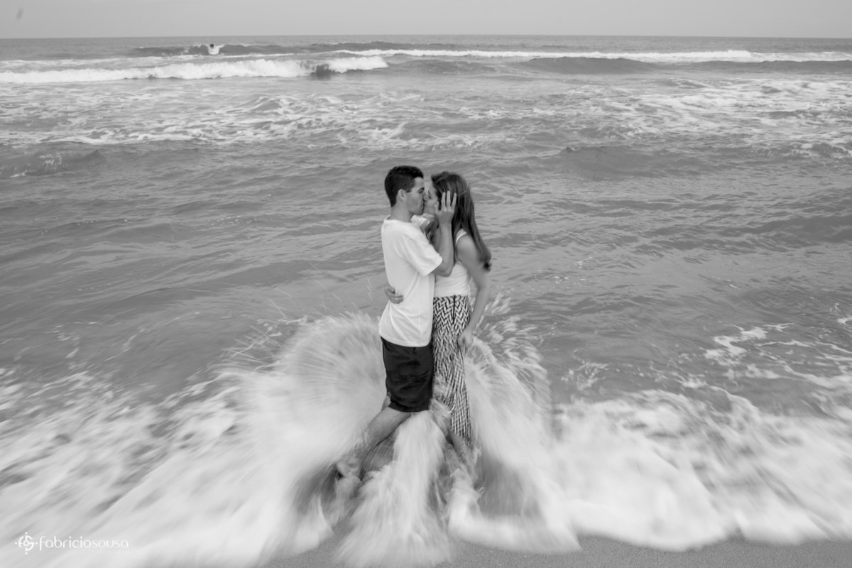 Pai e mãe se beijam na beira do mar com água nos pés