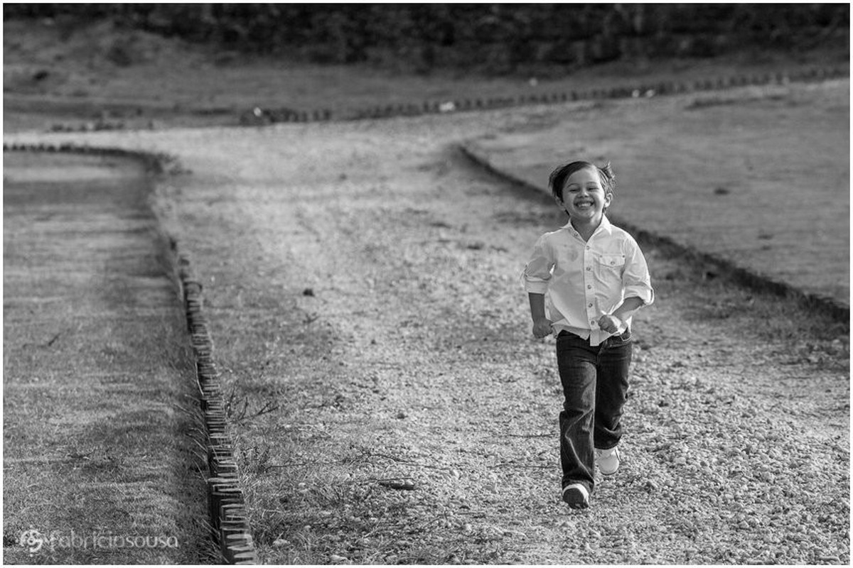 Menino corre feliz e sorridente por caminho de terra e grama