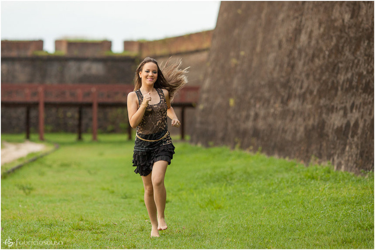 Ela corre no gramado em frente ao muro de pedra