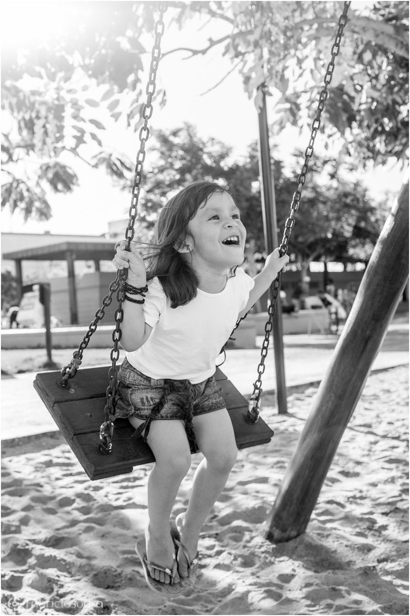 Criança brinca no balanço do parque na praça em sessão fotográfica infantil pb