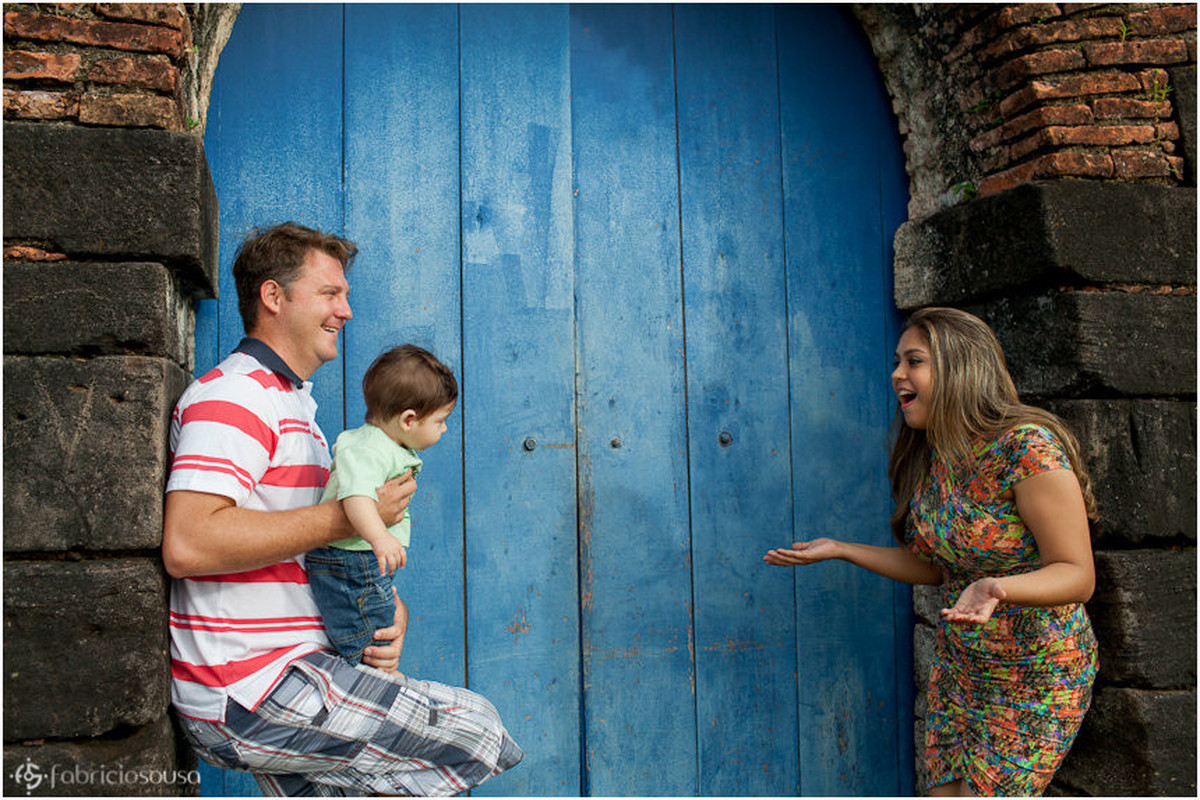 Família de 3 posam em frente à uma antiga porta azul de madeira