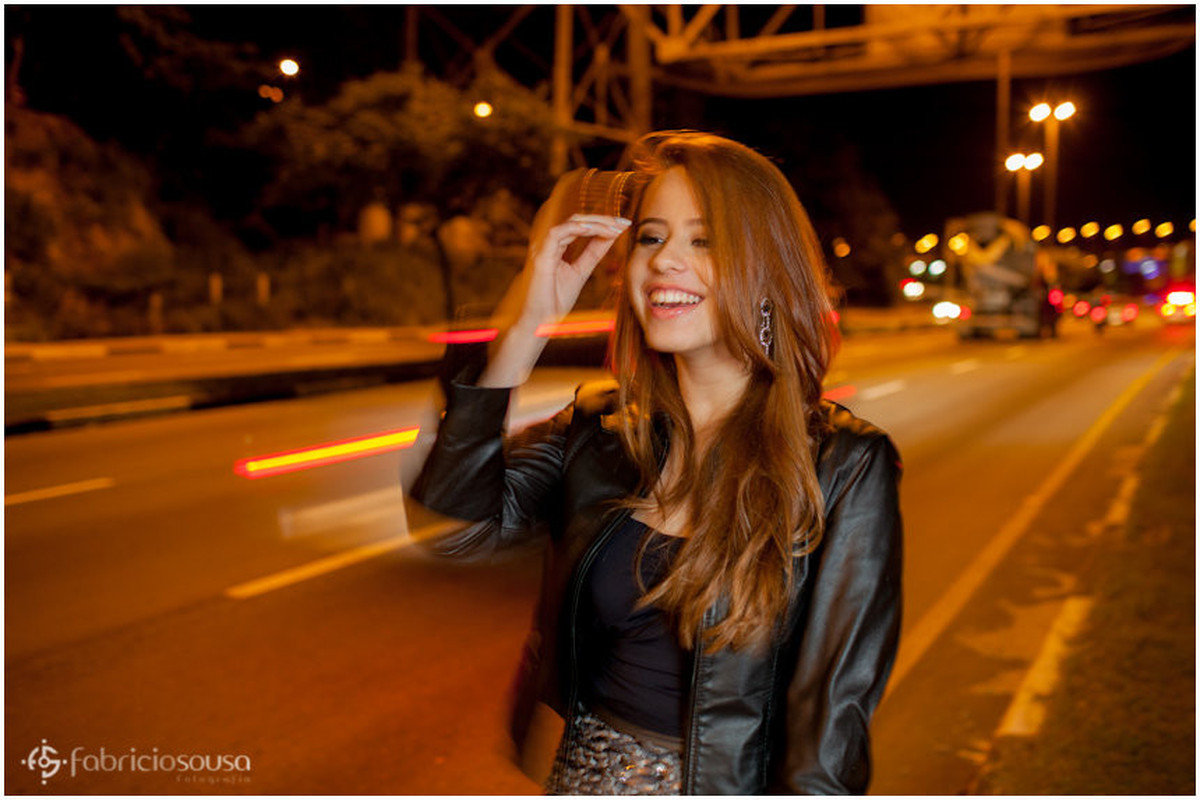 Nathalie sorri de jaqueta de couro próxima a ponte Hercílio Luz