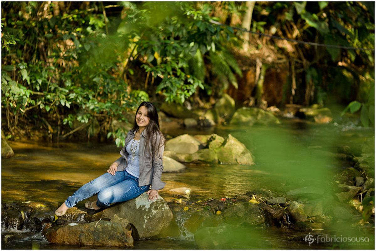 Menina-mulher sentada na pedra na beira do lago em ensaio fotográfico