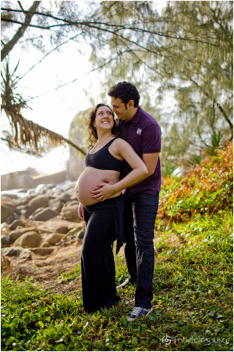 Namorado abraça namorada com as mãos na barriga da namorada e pedras ao fundo