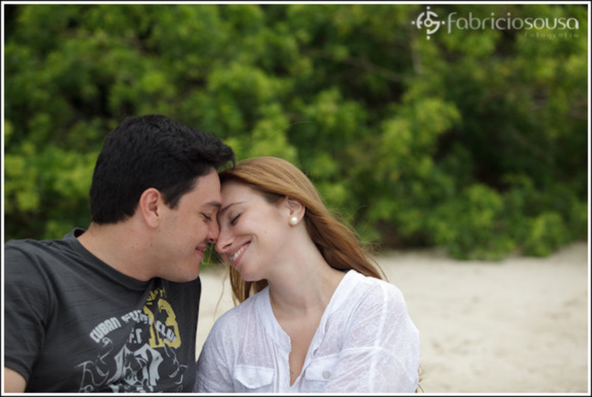 Casal de namorados sorrindo com rosto colado na areia da praia