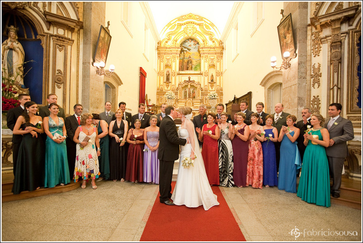 Casal de noivos recém casados se beijando à frente dos padrinhos e familiares na igreja