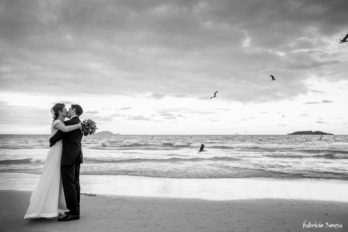 beijo do casal de noivos com gaivotes sobrevoando a praia