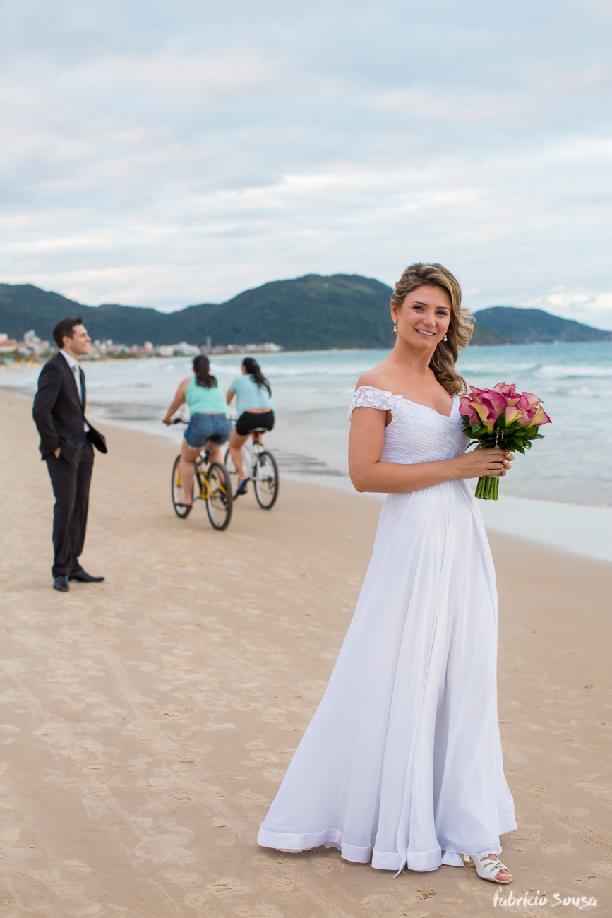 noiva com bouquet na praia - ciclistas passando na areia