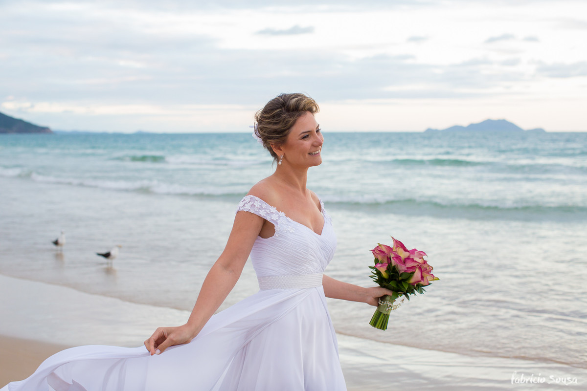 noiva maravilhosa segurando o vestido e o bouquet na beira do mar