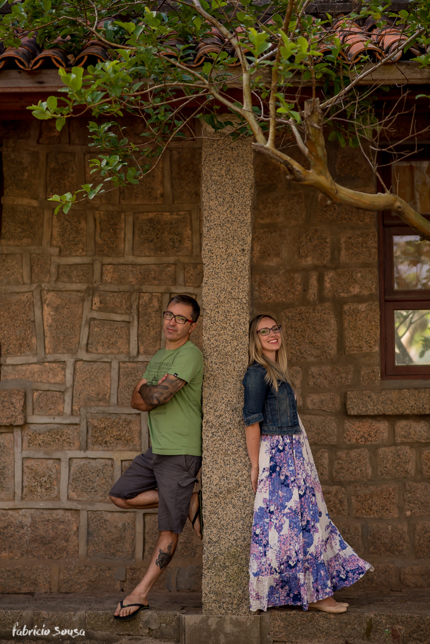 casal posa com muro de pedra e árvore singela no final do ensaio