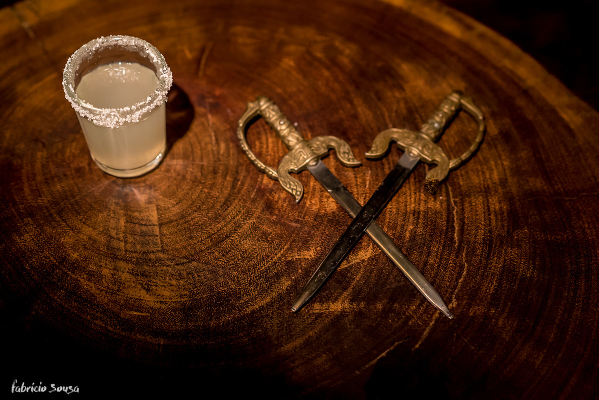 detalhe das espadas e shot de bebida no fundo de madeira rústica
