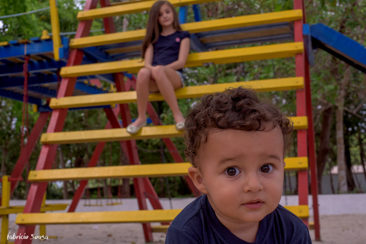 bebe olha diretamenta para câmera com sua irmã ao fundo