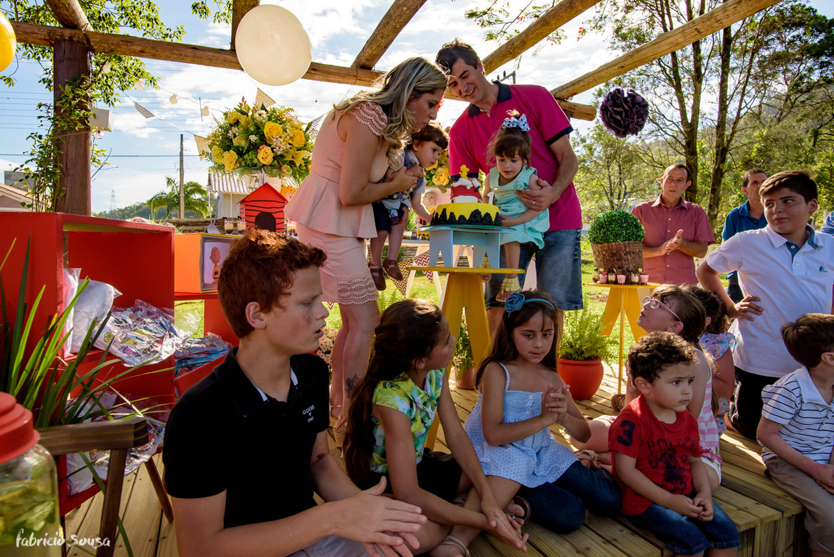 família assoprando as velinhas e crianças sentadas ao pé do bolo de aniversário infantil