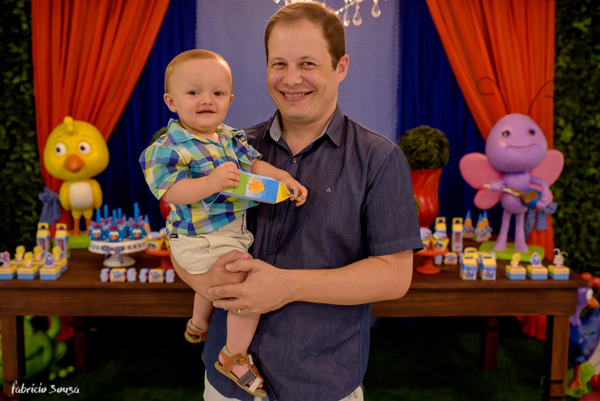 papai sorridente com bebe no colo no aniversário infantil