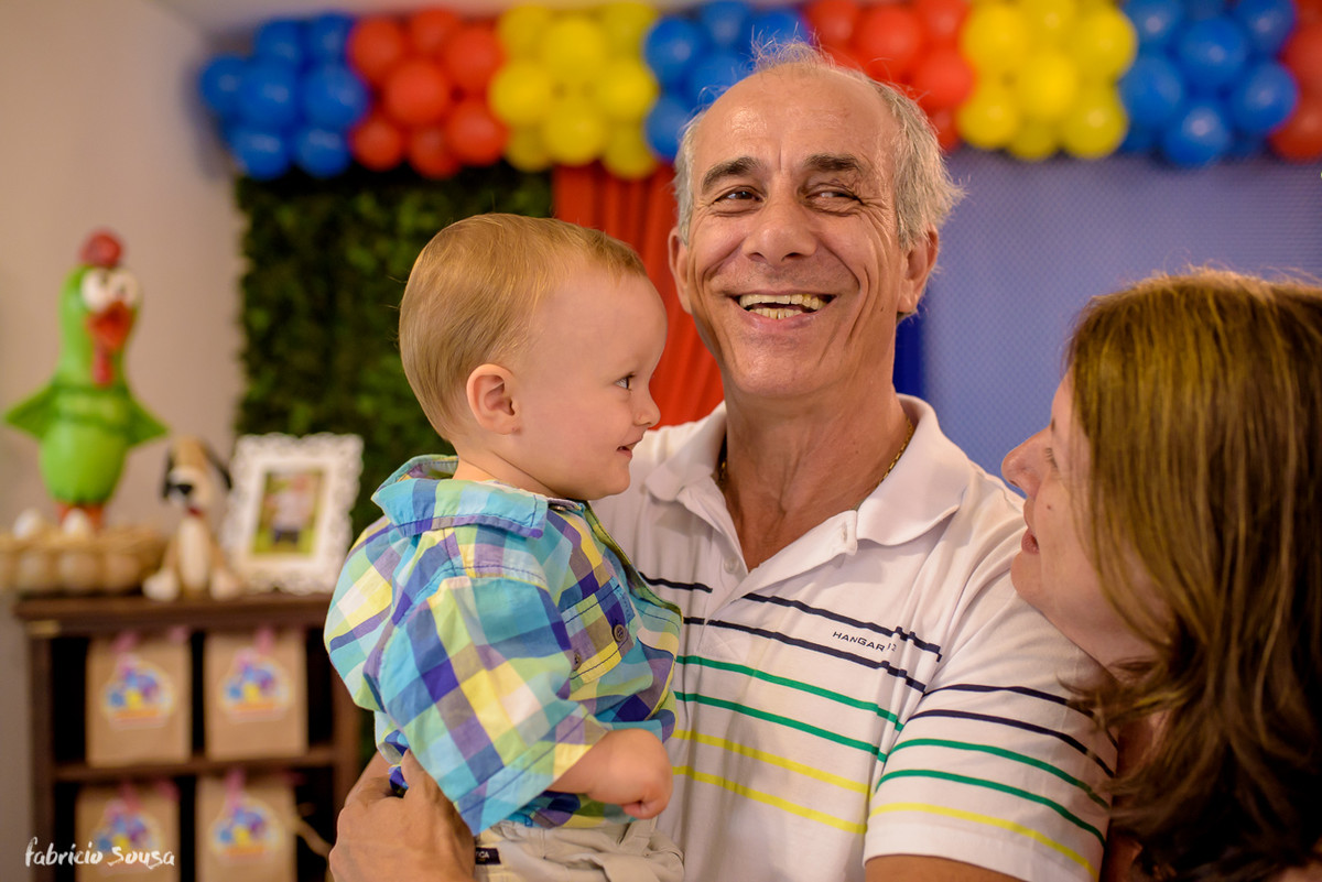 vovô todo orgulhoso e sorridente carregando seu neto Henrique no aniversário