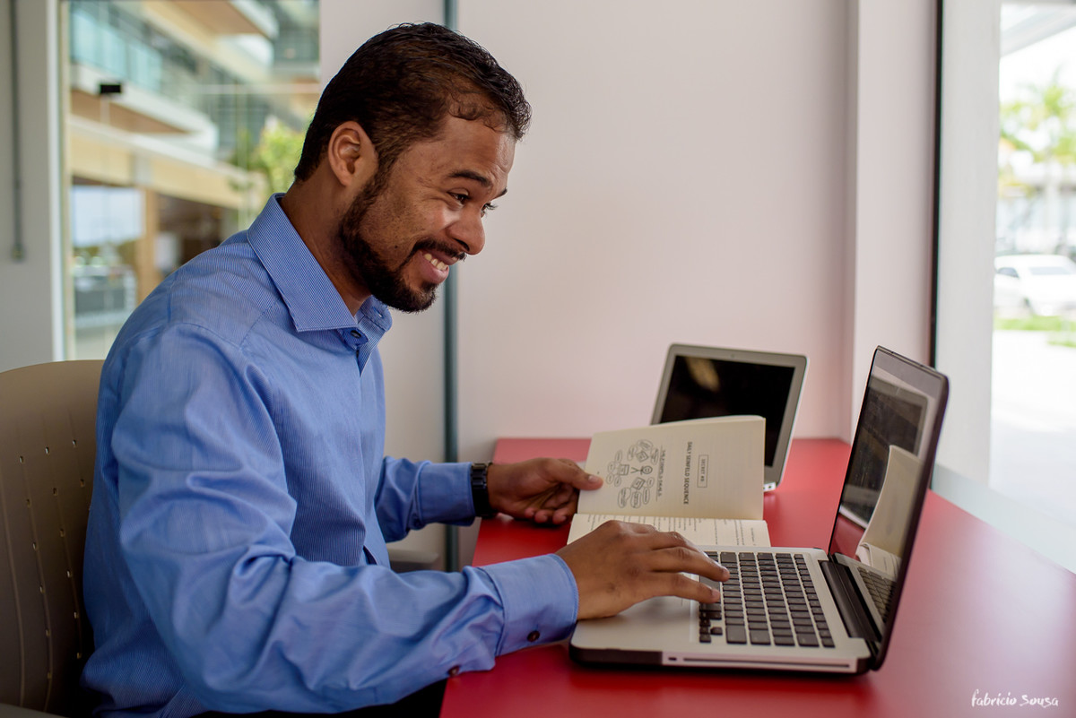 homem sorridente mexendo no computador e segurando um livro de marketing digital - dotcom secrets