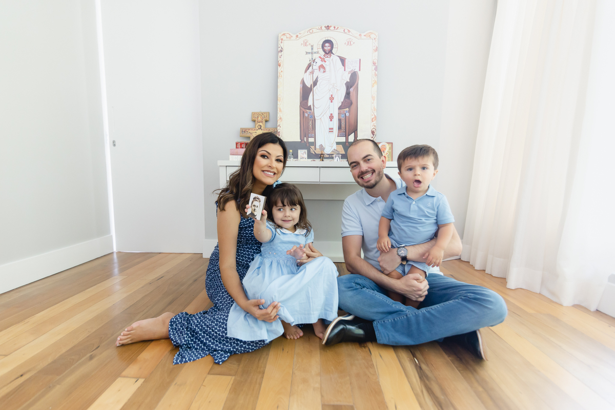 Pai e mãe sentados no chão e os filhos pequenos sentados no colo dos pais