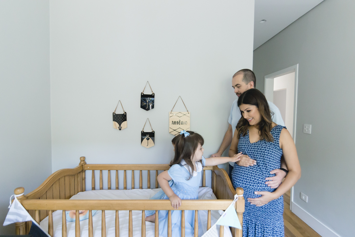 Criança em pé dentro do berço e fazendo carinho na barriga da mãe grávida