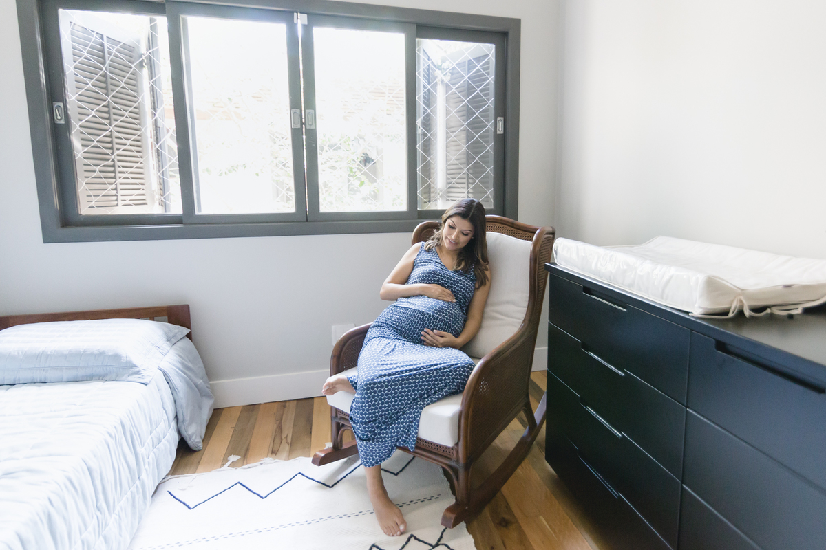 Mulher gestante com a mão na barriga sentada na poltrona de amamentação