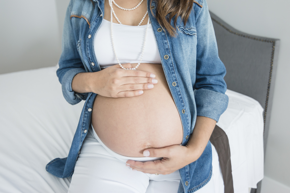 Barriga de mulher grávida sentada na beirada da cama