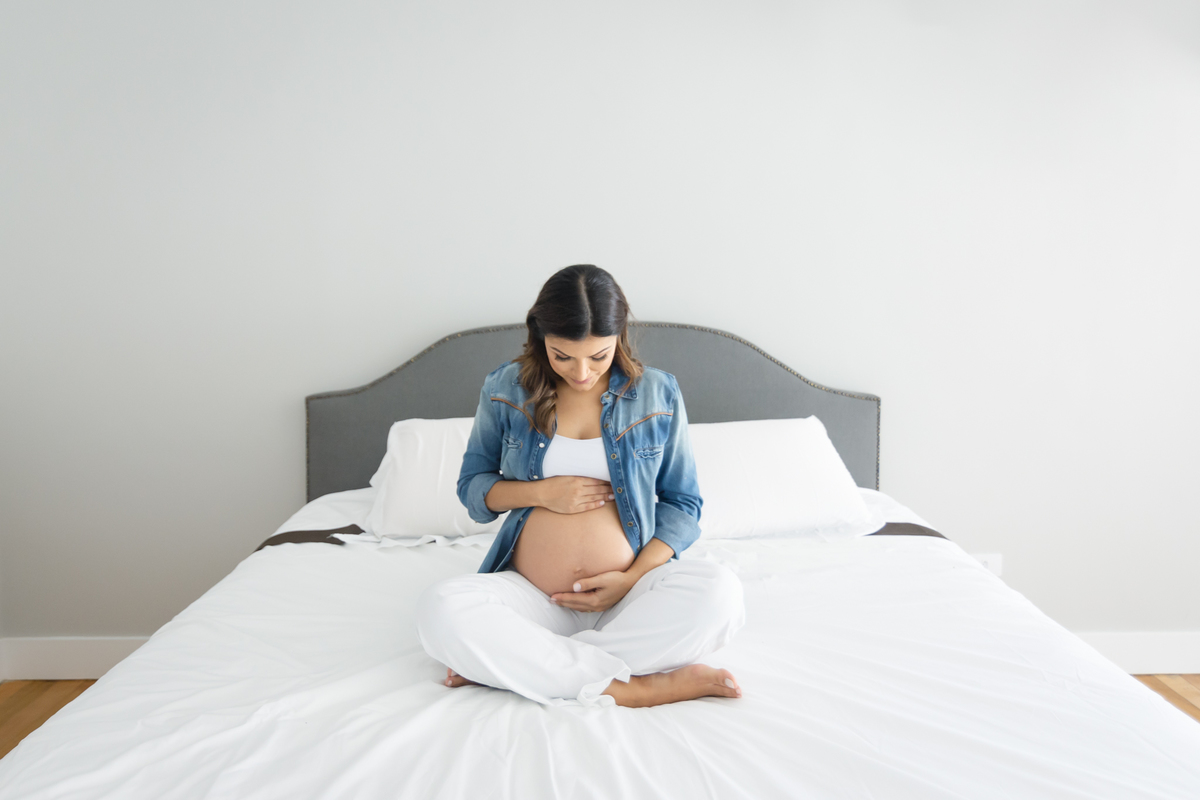 Mulher grávida sentada na cama olhando para a barriga