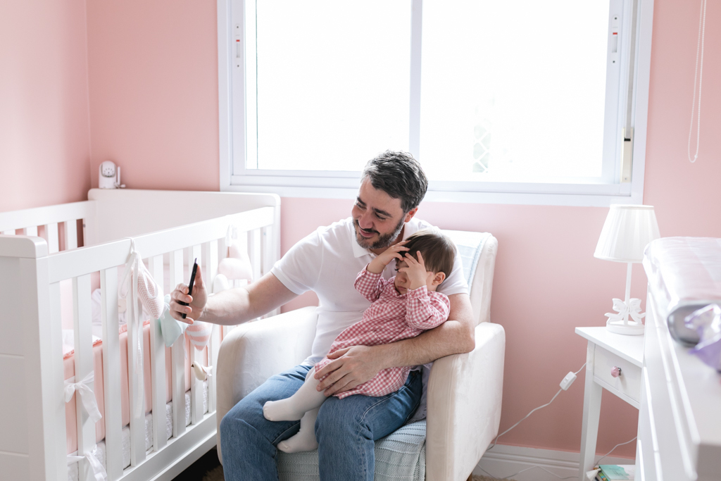 pai e filha sentados na poltrona do quarto e fazendo video chamada