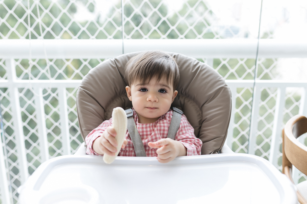 bebe sentada em cadeirão segurando uma banana 