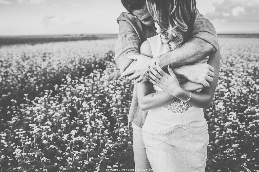 O casal se abraça em fotografia preto e branca tirada pelo fotógrafo profissional de casamentos no ensaio de namorados em plantação de trigo sarraceno em Brasília – DF