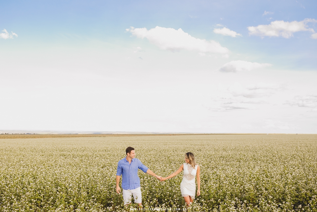 Casal de mãos dadas com céu azul em ensaio de noivos
