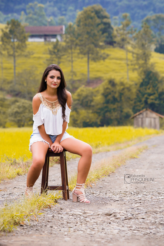 Fotografada, Aline sentada em banquinho numa estrada de interior. Fotografia de Eduardo Pasqualini, fotógrafo de casamentos e ensaios em Rio do Sul, Santa Catarina.