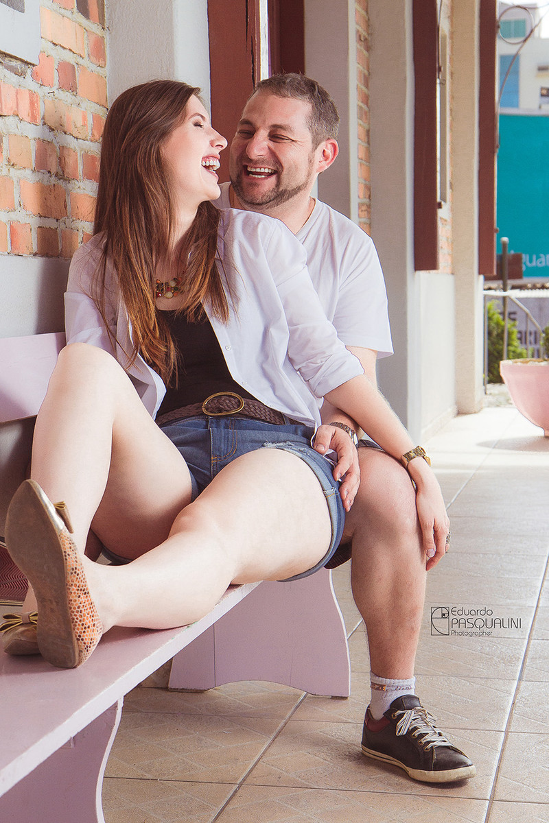 Sentados em banco rosa, casal sorrindo. Fotografia de Eduardo Pasqualini, fotógrafo de casamentos e ensaios em Rio do Sul, Santa Catarina.