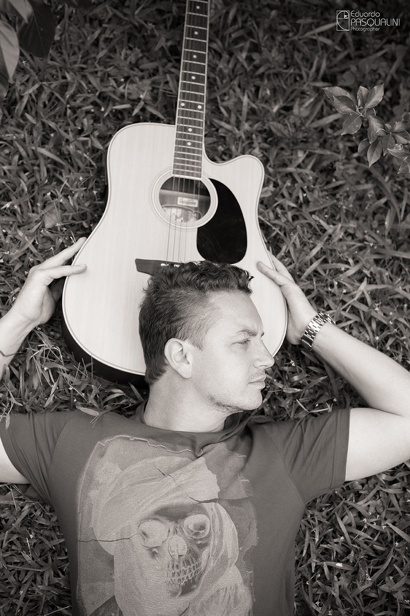 Deitado na grama com a cabeça apoiada no violão. Homem. Foto de Eduardo Pasqualini, fotógrafo de casamentos e ensaios em Rio do Sul, Santa Catarina.