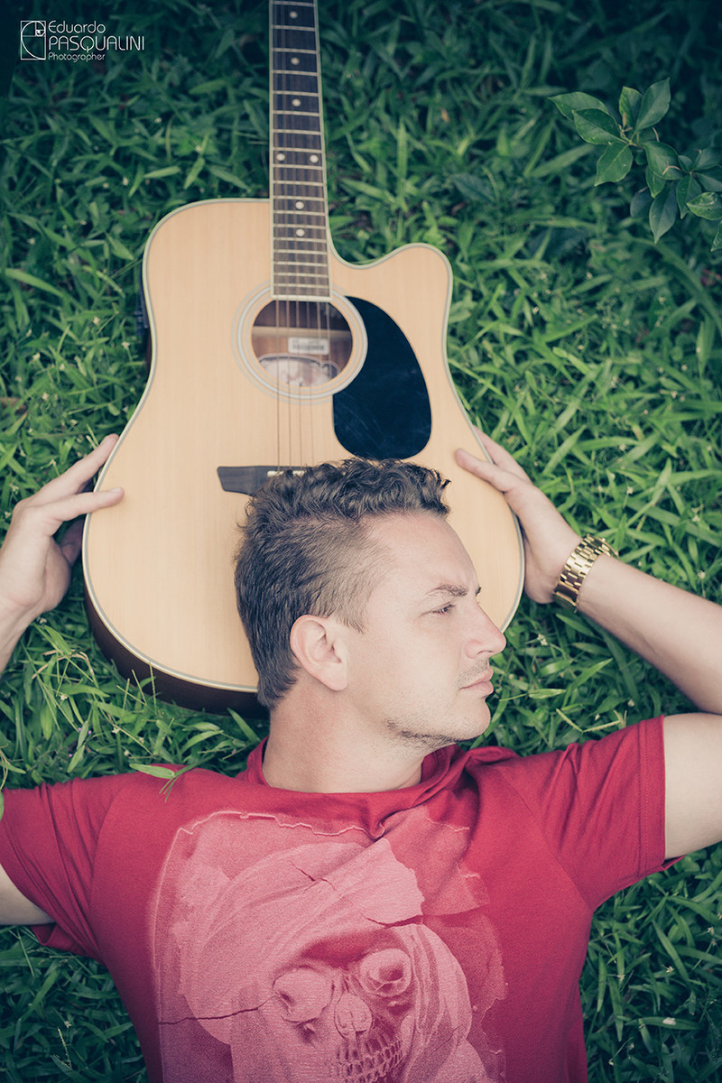 Rapaz deitado na grama com a cabeça apoiada no violão. Foto de Eduardo Pasqualini, fotógrafo de casamentos e ensaios em Rio do Sul, Santa Catarina.