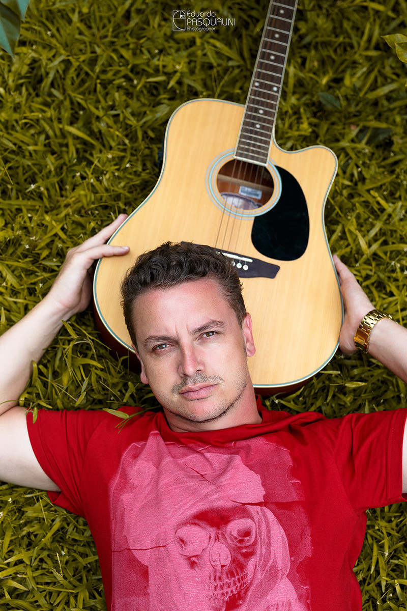 Na grama com a cabeça apoiada no violão, homem olhando para a câmera. Foto de Eduardo Pasqualini, fotógrafo de casamentos e ensaios em Rio do Sul, Santa Catarina.